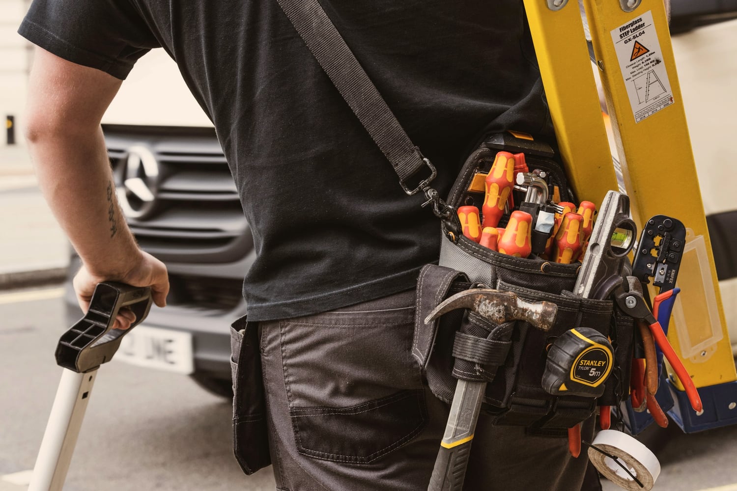 Tradesperson with a loaded tool belt and ladder on a job